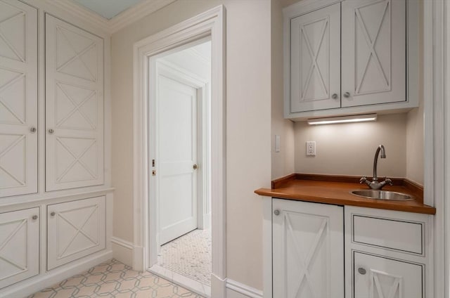 bar featuring indoor wet bar, a sink, baseboards, and light tile patterned floors