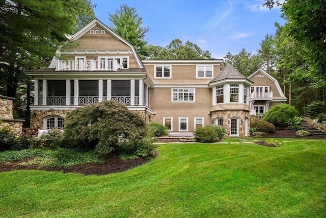 back of house featuring stone siding, a balcony, a sunroom, and a gambrel roof
