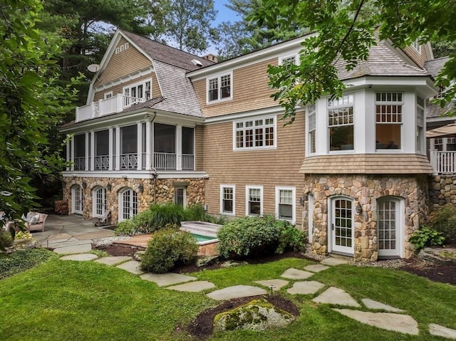 back of house with a lawn, a patio area, a balcony, and stone siding