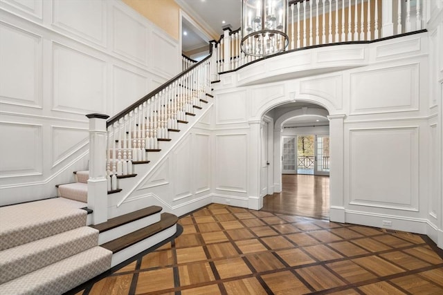 staircase with arched walkways, a high ceiling, a decorative wall, and a notable chandelier