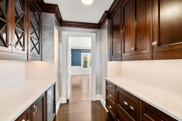 bar featuring crown molding, baseboards, a decorative wall, and dark wood-style floors
