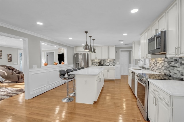 kitchen with pendant lighting, white cabinets, light hardwood / wood-style floors, a kitchen island, and stainless steel appliances