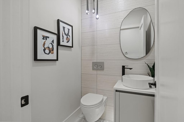 half bath featuring tile walls, vanity, toilet, tile patterned floors, and baseboards