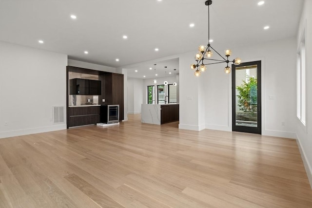 unfurnished living room featuring wine cooler, a chandelier, light wood-type flooring, recessed lighting, and a sink