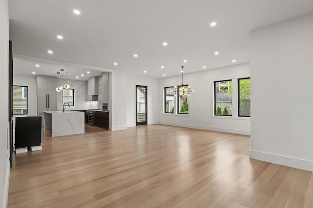 unfurnished living room featuring a chandelier, light wood finished floors, recessed lighting, baseboards, and a sink