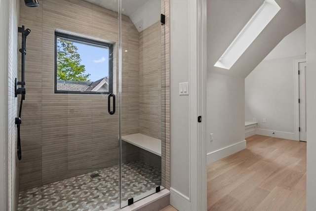 bathroom featuring vaulted ceiling, a shower stall, wood finished floors, a skylight, and baseboards