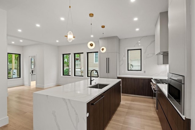 kitchen with a sink, modern cabinets, high end stainless steel range oven, oven, and light wood-type flooring
