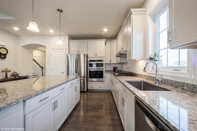 kitchen featuring arched walkways, under cabinet range hood, white cabinets, a sink, and stainless steel appliances