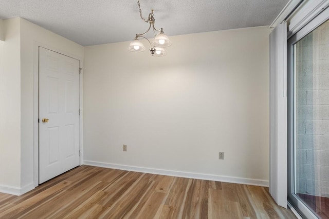 empty room featuring a notable chandelier, light wood-type flooring, and a textured ceiling