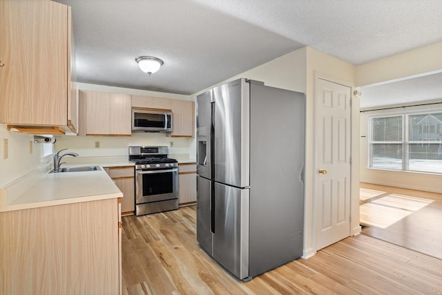 kitchen with light brown cabinetry, a textured ceiling, stainless steel appliances, sink, and light hardwood / wood-style floors