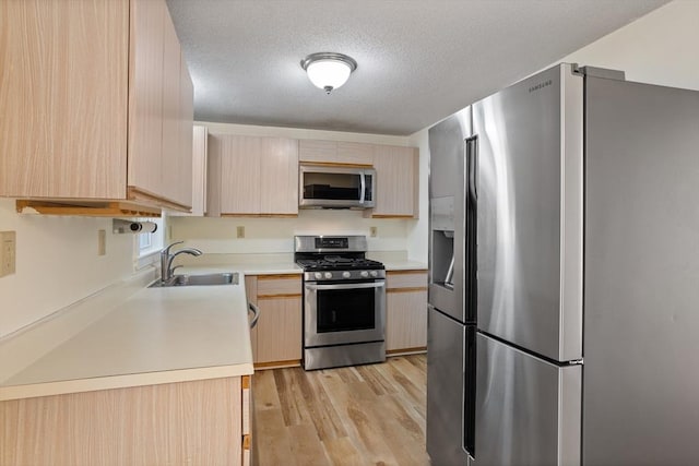 kitchen with sink, stainless steel appliances, light hardwood / wood-style flooring, a textured ceiling, and light brown cabinetry