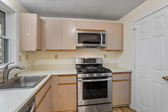 kitchen with a textured ceiling, sink, light brown cabinets, and appliances with stainless steel finishes