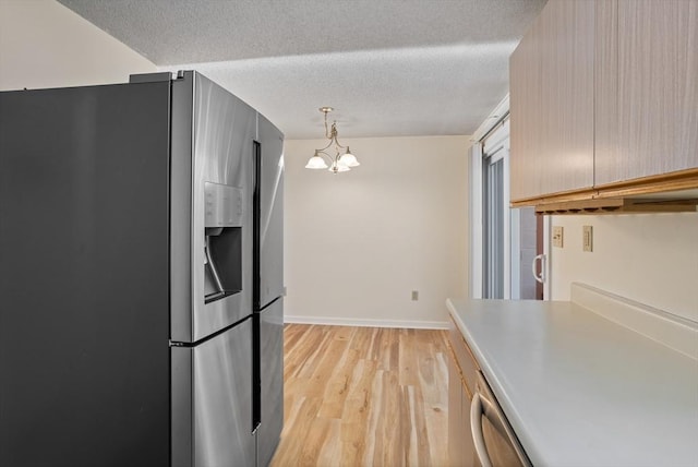 kitchen with light wood-type flooring, a textured ceiling, decorative light fixtures, stainless steel appliances, and a chandelier