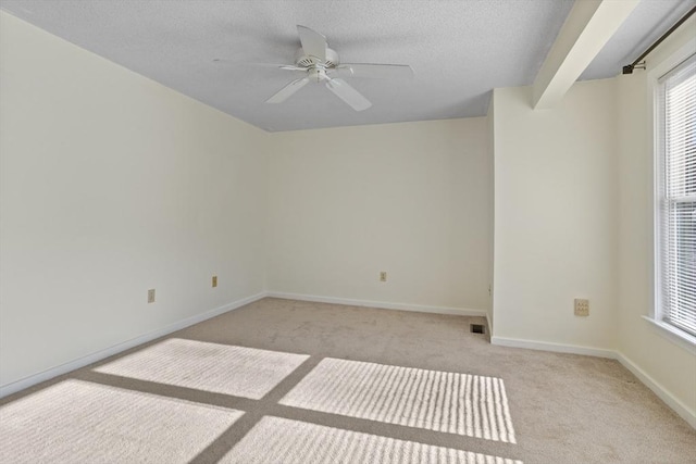 empty room featuring beamed ceiling, ceiling fan, and light colored carpet