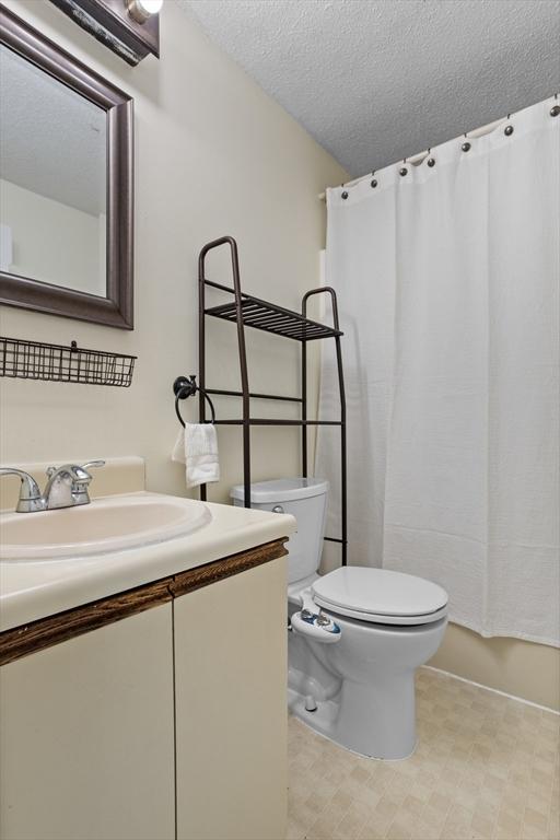 full bathroom with vanity, toilet, a textured ceiling, and shower / tub combo with curtain