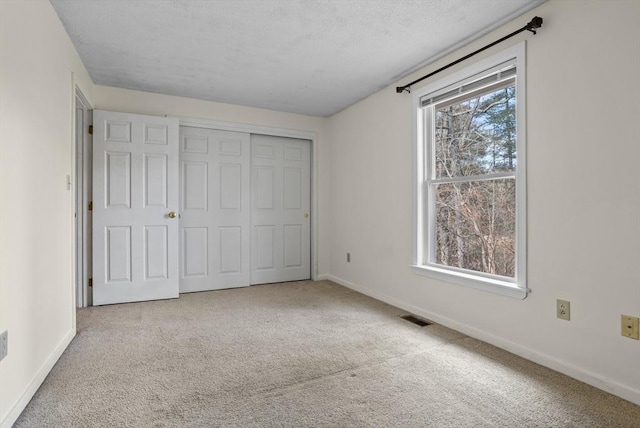 unfurnished bedroom featuring a textured ceiling, light colored carpet, and a closet