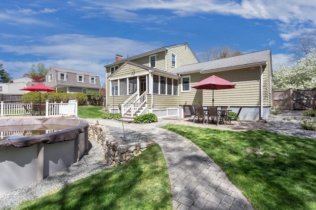 rear view of house featuring a chimney, a yard, fence, a patio area, and a sunroom