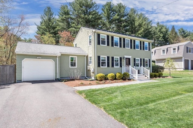 colonial home with fence, a garage, a front lawn, and driveway