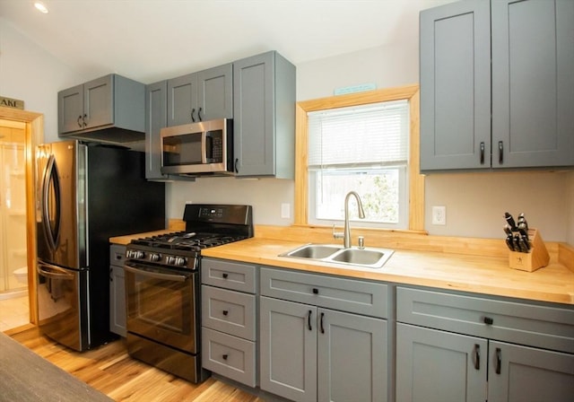 kitchen with stainless steel appliances, gray cabinetry, a sink, wood counters, and light wood-type flooring