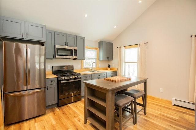 kitchen with baseboard heating, stainless steel appliances, light countertops, light wood-style floors, and a sink