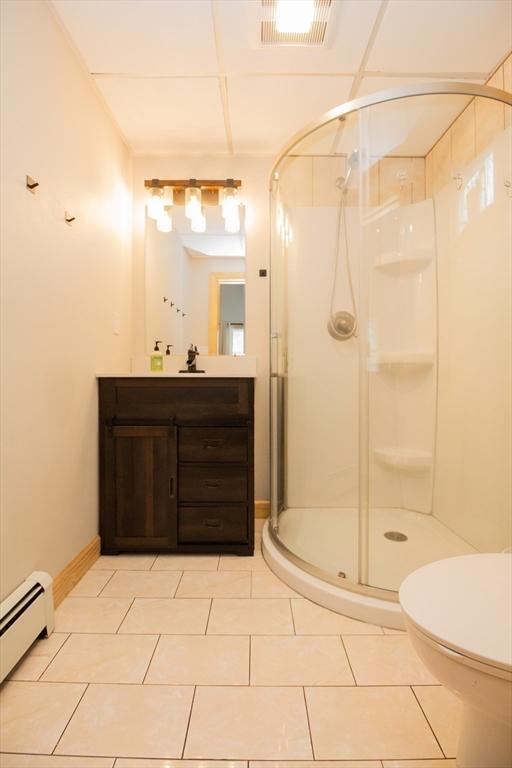 full bathroom featuring visible vents, toilet, a baseboard heating unit, a stall shower, and vanity