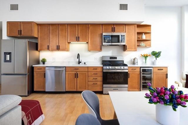 kitchen featuring sink, light hardwood / wood-style flooring, beverage cooler, and appliances with stainless steel finishes