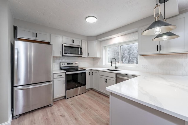 kitchen featuring decorative light fixtures, sink, light stone countertops, stainless steel appliances, and white cabinets