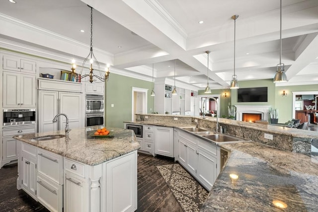 kitchen with open floor plan, built in appliances, a sink, and a large island with sink