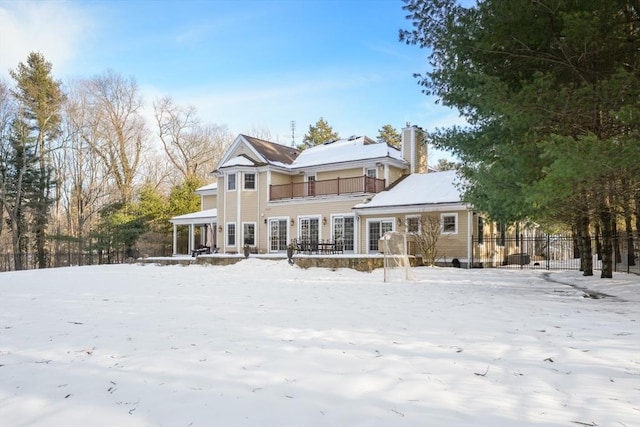 snow covered property with a chimney, fence, and a balcony