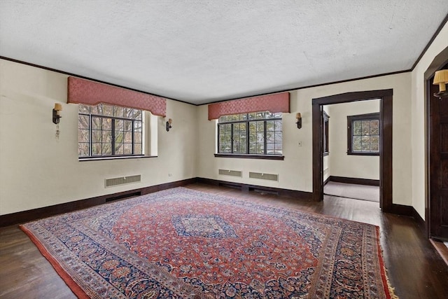 unfurnished room featuring crown molding, visible vents, a textured ceiling, wood finished floors, and baseboards