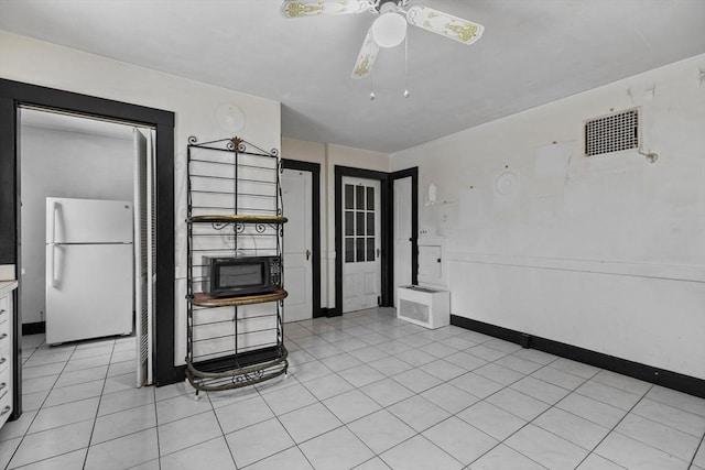 kitchen featuring light tile patterned floors, baseboards, ceiling fan, freestanding refrigerator, and black microwave