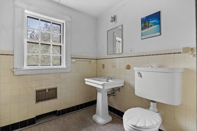 bathroom featuring toilet, tile walls, visible vents, wainscoting, and tile patterned floors