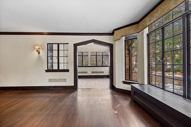 empty room featuring a wealth of natural light, ornamental molding, wood finished floors, and visible vents