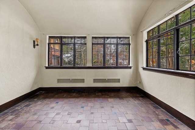 empty room featuring visible vents, vaulted ceiling, and baseboards