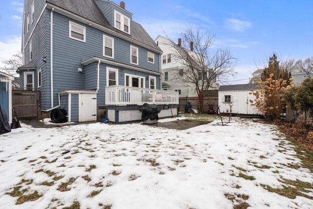 snow covered rear of property with a storage shed and a deck