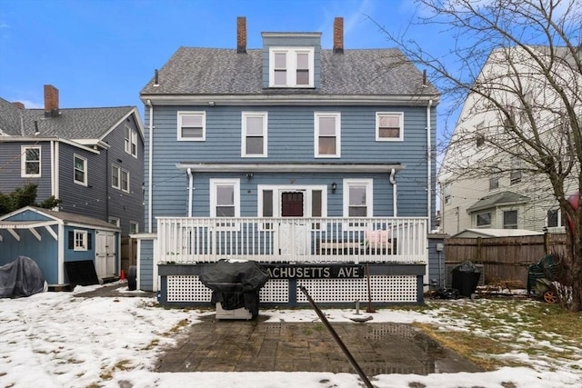 snow covered rear of property featuring a storage shed and a deck