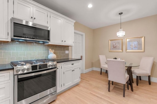 kitchen with light hardwood / wood-style flooring, hanging light fixtures, appliances with stainless steel finishes, decorative backsplash, and white cabinets