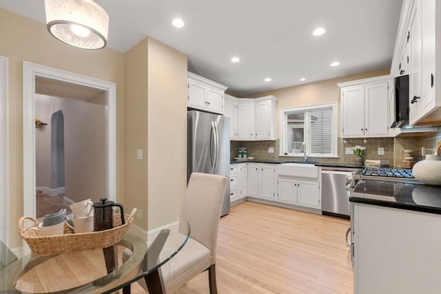 kitchen with appliances with stainless steel finishes, sink, white cabinets, decorative backsplash, and light hardwood / wood-style floors