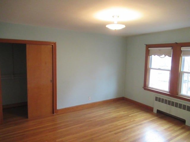 unfurnished bedroom featuring a closet, light wood-type flooring, radiator heating unit, and baseboards