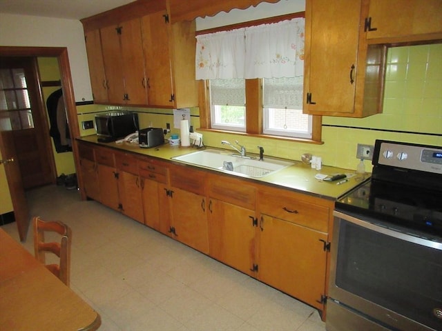 kitchen featuring backsplash, stainless steel electric stove, light floors, brown cabinets, and a sink