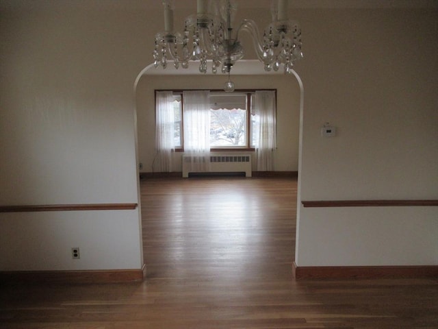 unfurnished room with arched walkways, radiator, an inviting chandelier, and wood finished floors