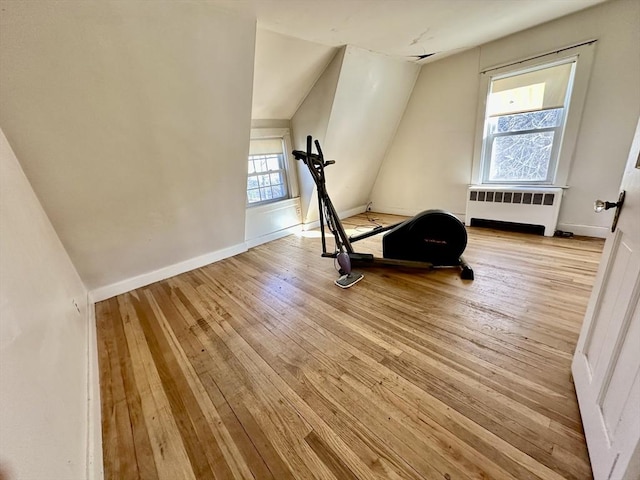 exercise area featuring a healthy amount of sunlight, vaulted ceiling, radiator, and light hardwood / wood-style flooring