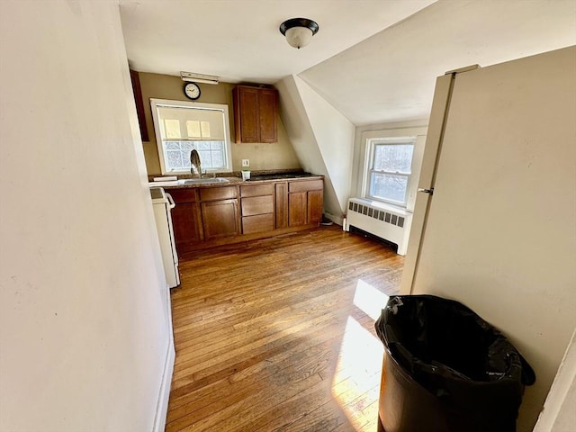 kitchen featuring radiator, sink, light hardwood / wood-style floors, lofted ceiling, and range