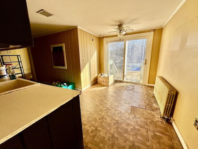 interior space featuring ceiling fan, radiator heating unit, sink, wood walls, and ornamental molding