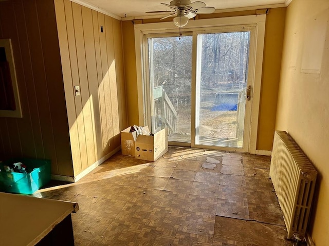 entryway featuring radiator heating unit, wooden walls, ceiling fan, and crown molding