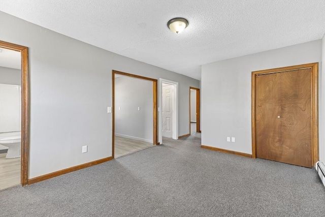 unfurnished bedroom featuring light carpet, a textured ceiling, a baseboard heating unit, and ensuite bath