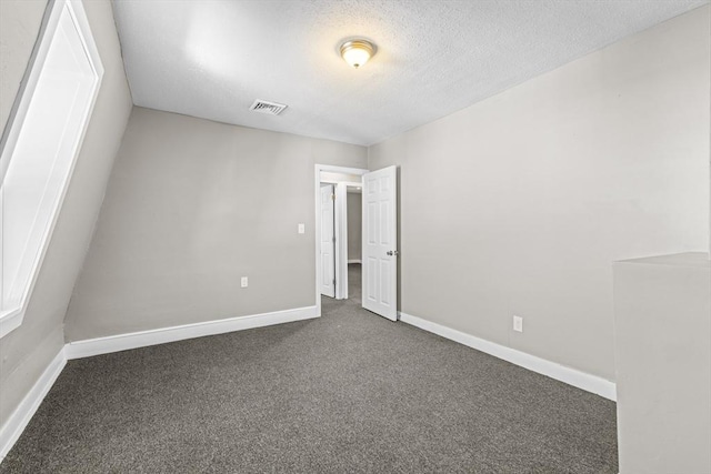 empty room with a textured ceiling and dark colored carpet