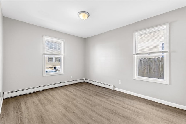 spare room featuring baseboard heating and light hardwood / wood-style floors