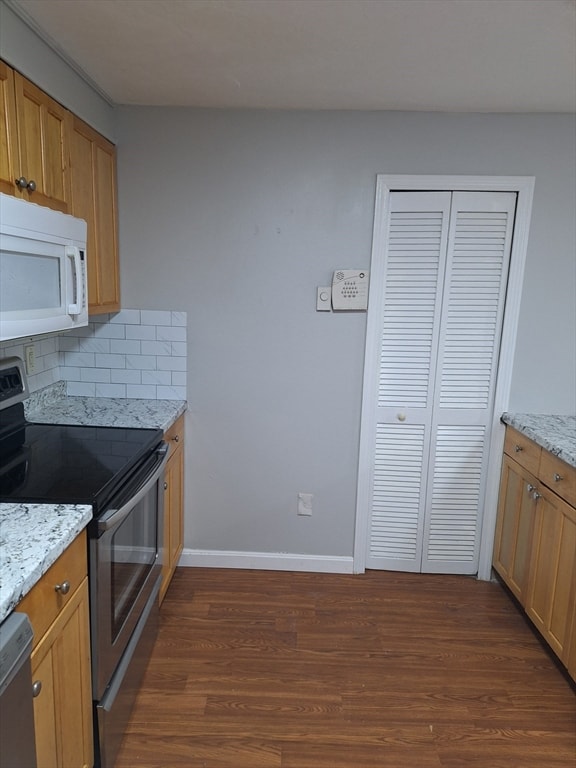 kitchen with decorative backsplash, light stone counters, stainless steel appliances, and dark hardwood / wood-style flooring