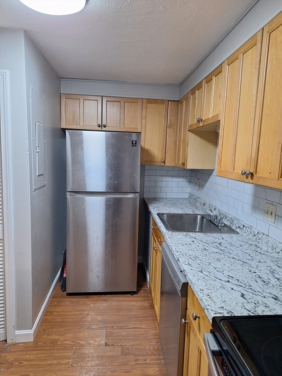 kitchen with stainless steel appliances, tasteful backsplash, sink, and light wood-type flooring